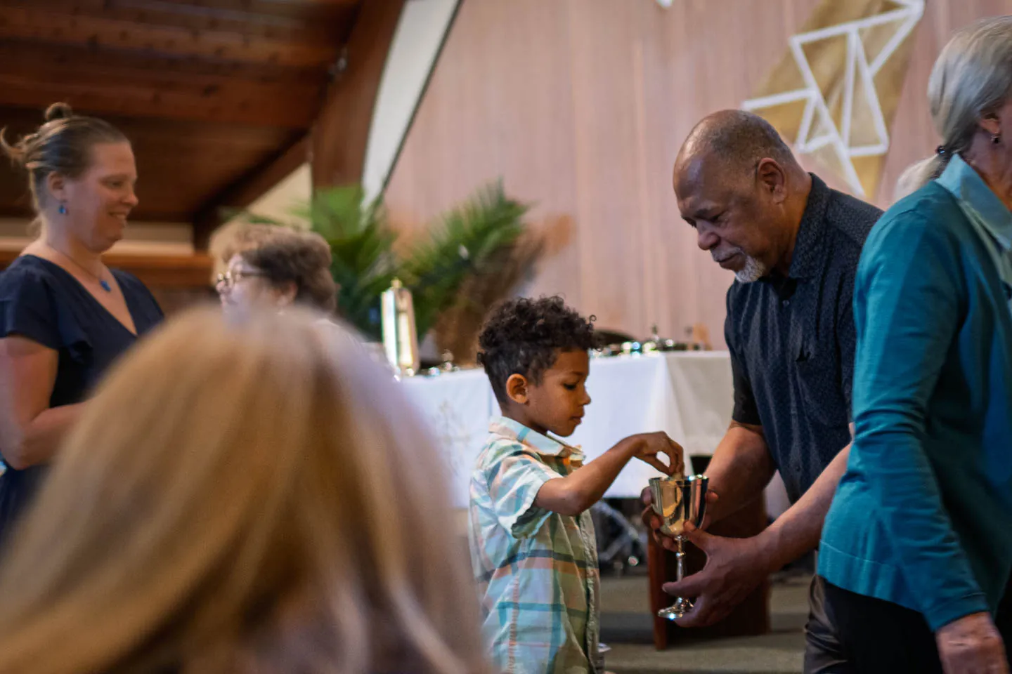 A young boy dips bread into a communion chalice held by an older man during a service