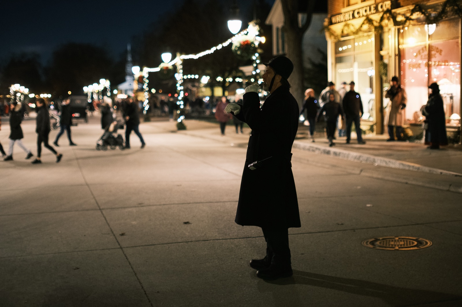 A costumed night watchman blows a whistle on a lamplit street at Christmastime
