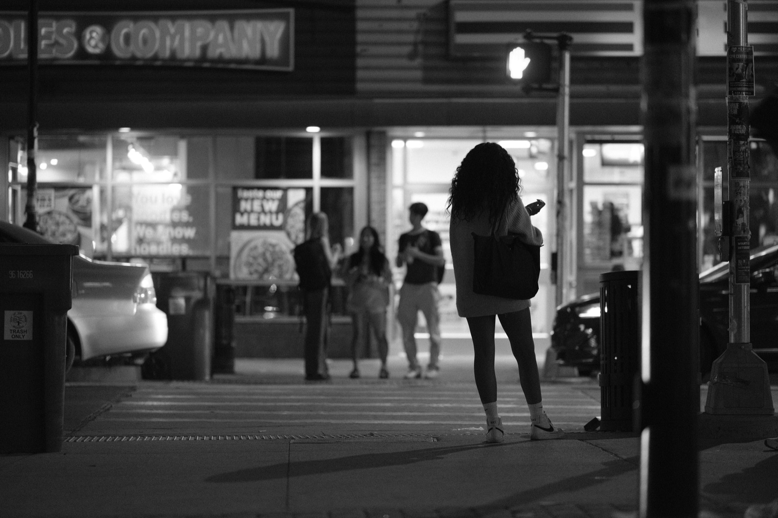 A woman checks her phone at a night crosswalk, black and white