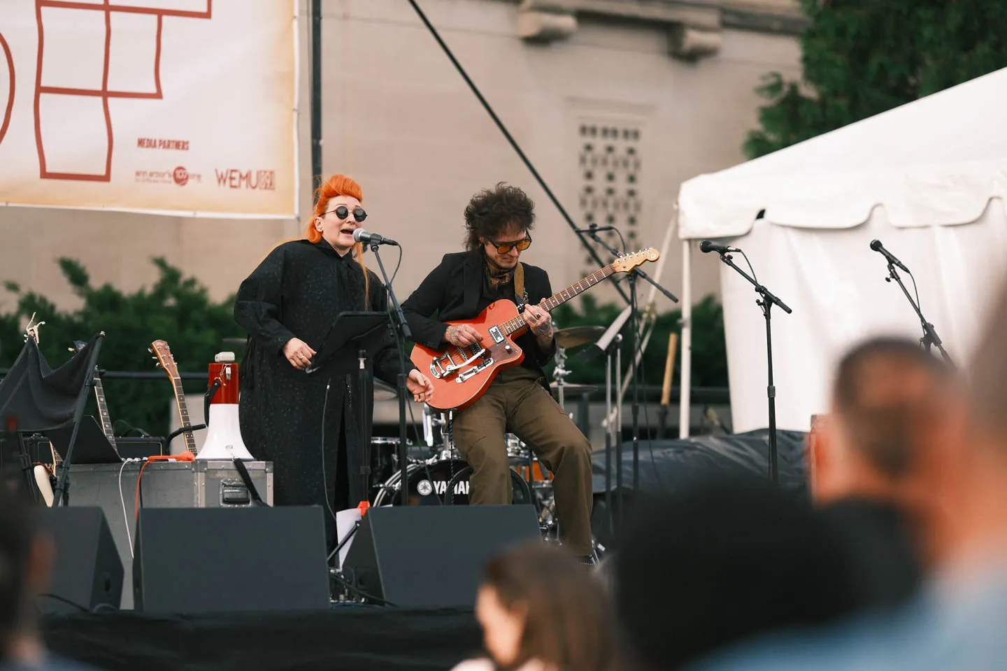 A singer and guitarist play an outdoor festival stage at dusk